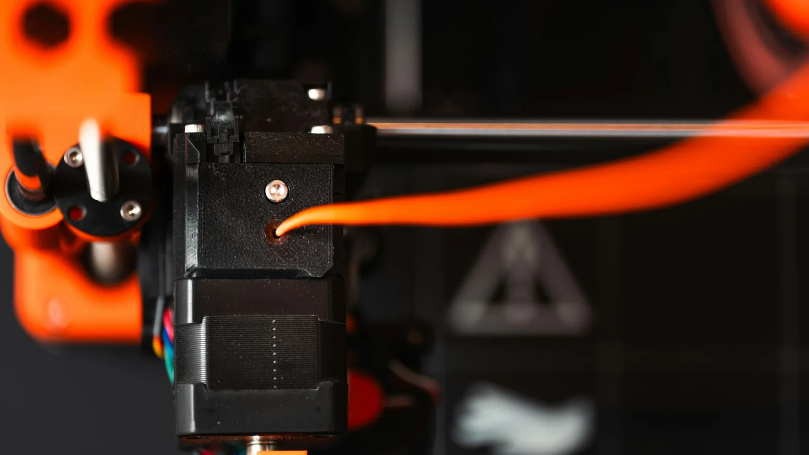 Close-up of a 3D printer head feeding orange plastic filament