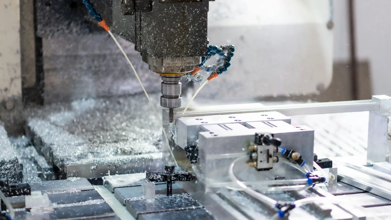 CNC machine milling an aluminium part, with coolant spraying and metal chips around the cutter