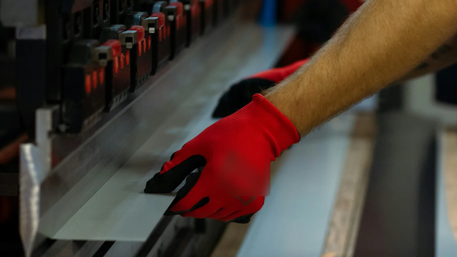 Gloved hands feeding a metal sheet into a press brake to bend it